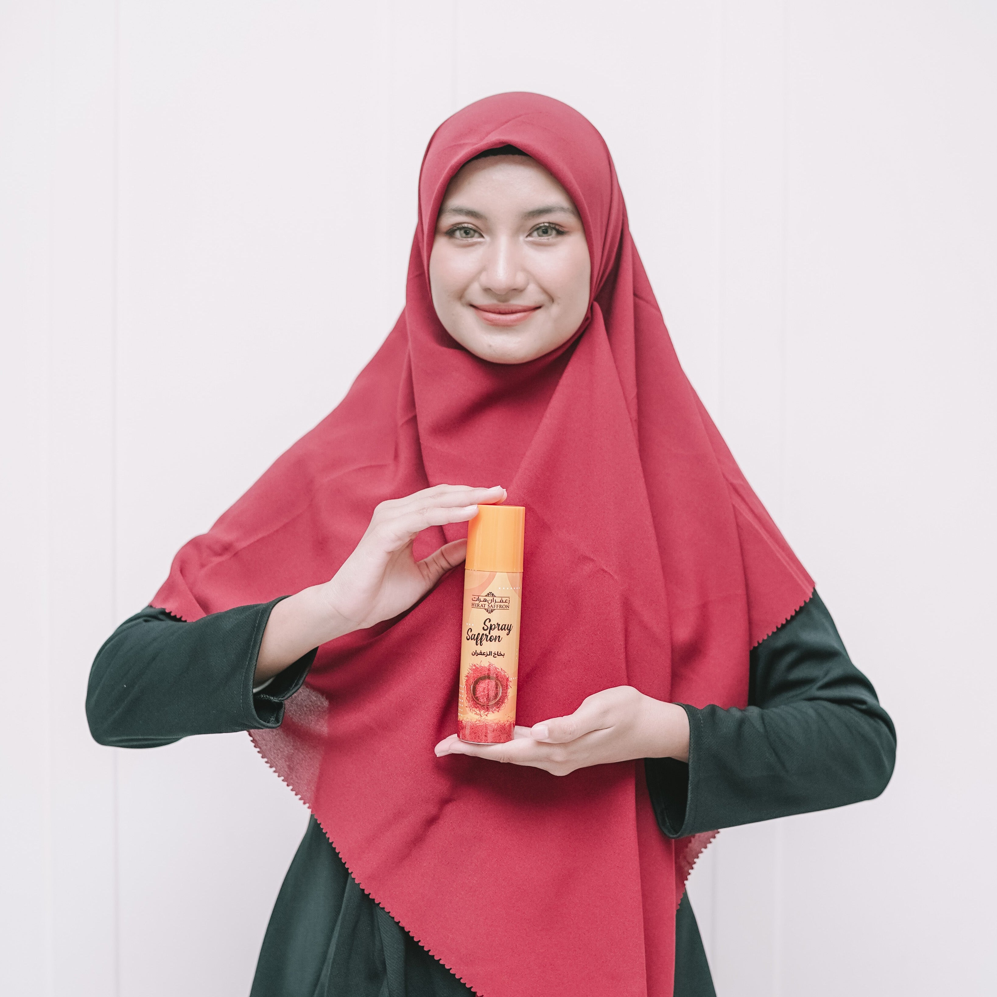 Person wearing a red hijab holding a product against a white background