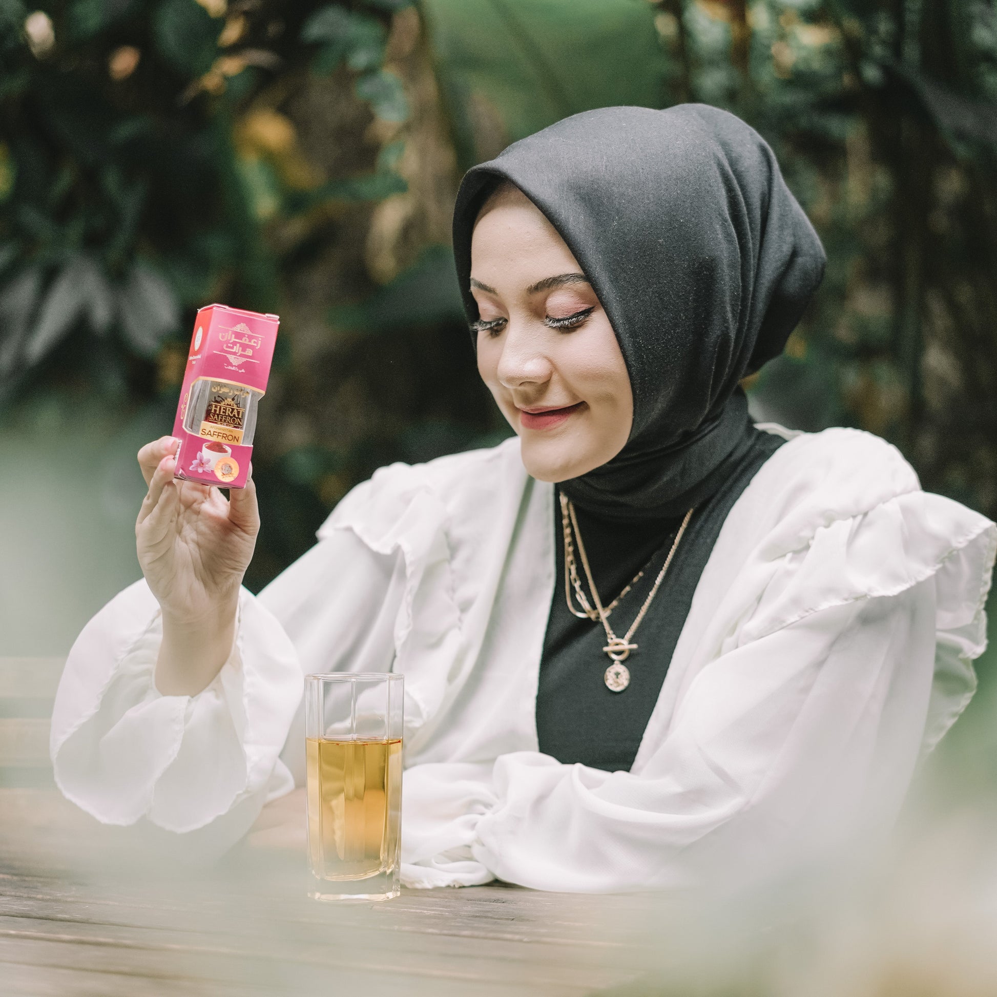 Woman holding a pink product package outdoors with greenery in the background