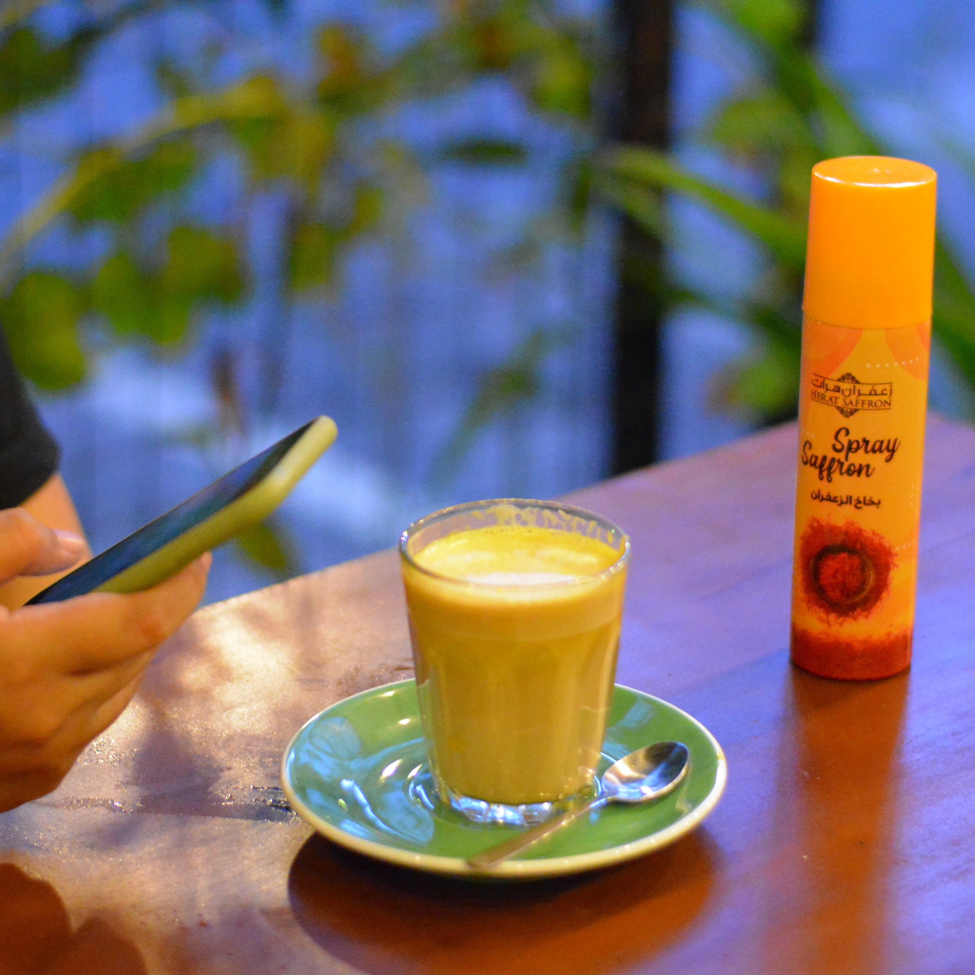 Person using a phone with a glass of yellow drink and a bottle on a table.