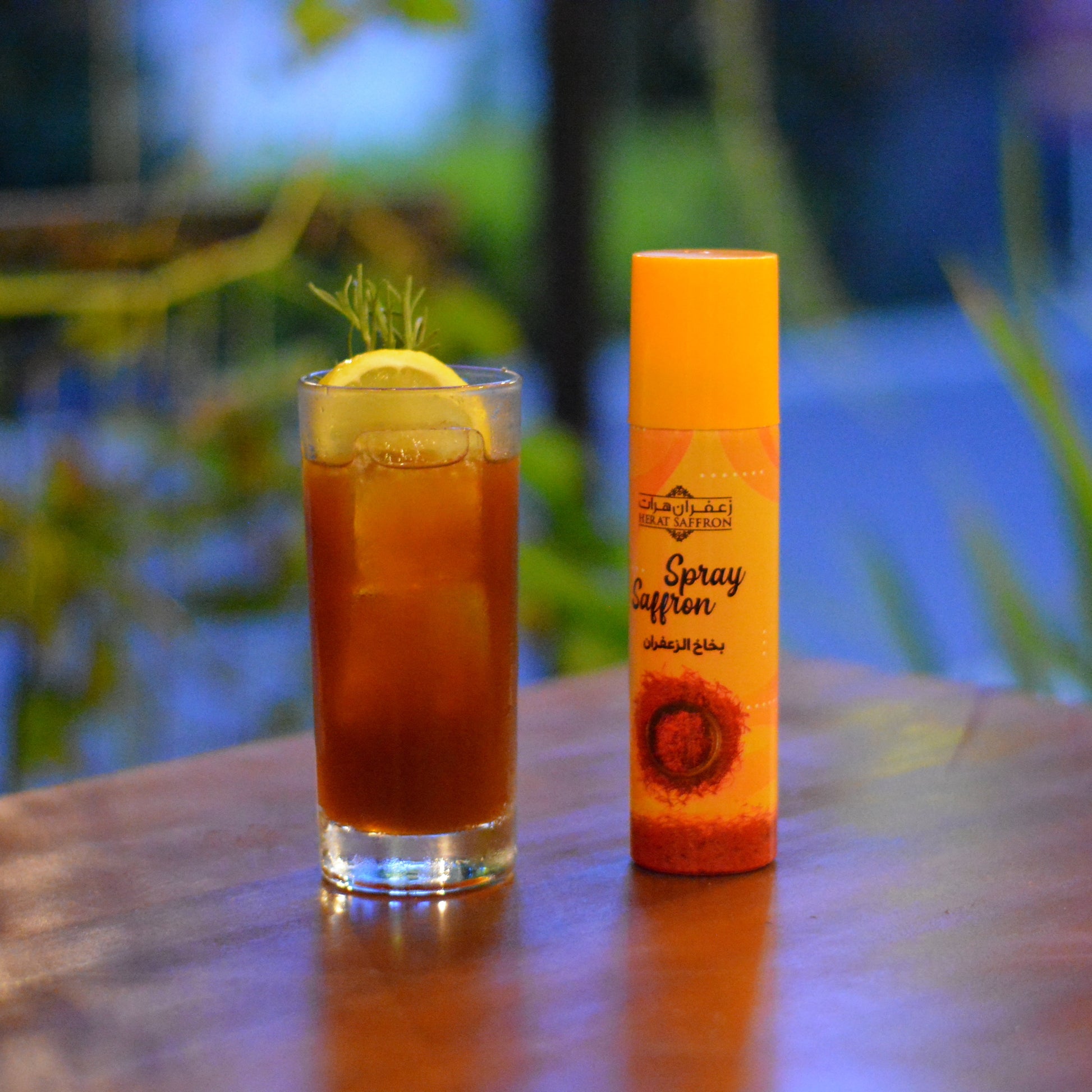 Glass of iced tea with a bottle of 'Spray & Sip' on a wooden table outdoors.