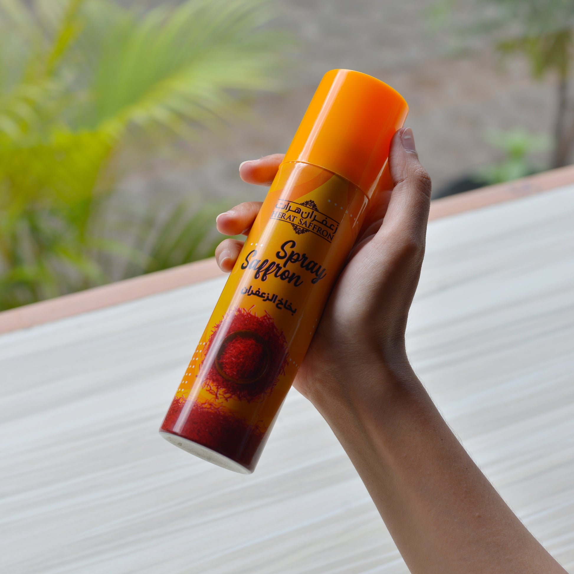 Hand holding an orange spray can with a blurred outdoor background